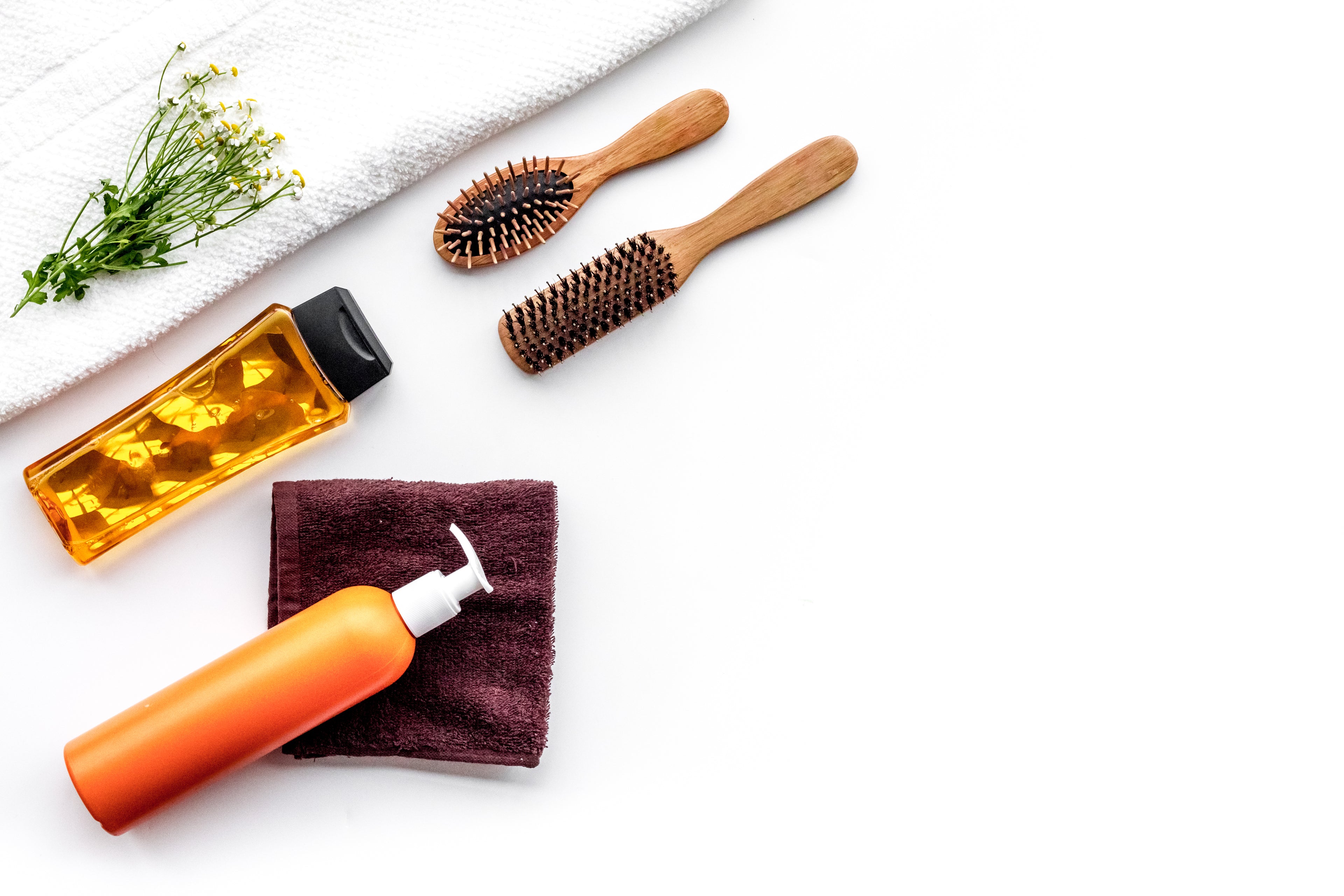 Two hair brushes, a large towel, hand pump on a maroon hand towel and bottle with hair gels, on a crisp white background.